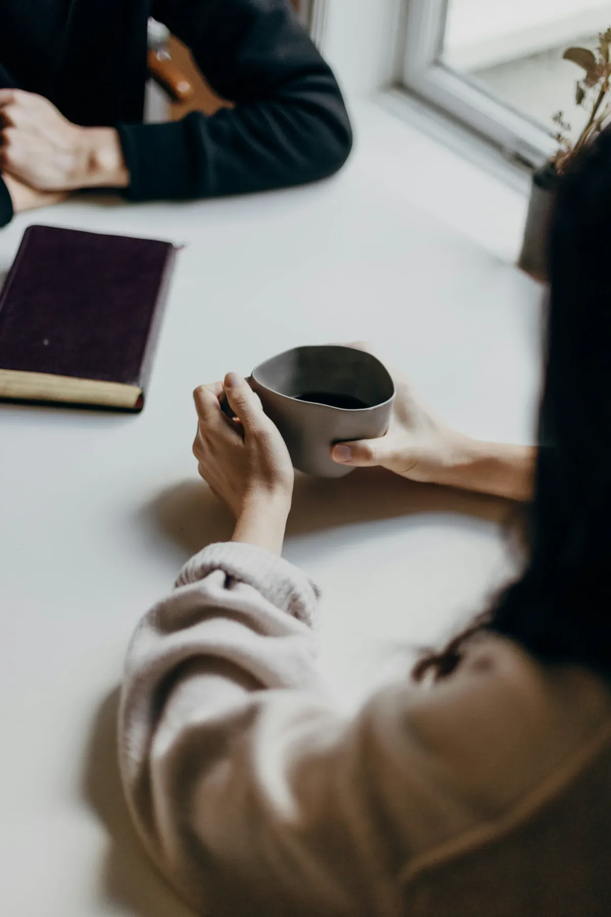 Zwei Personen im Gespräch an einem hellen Tisch, davor Kaffee und ein Buch