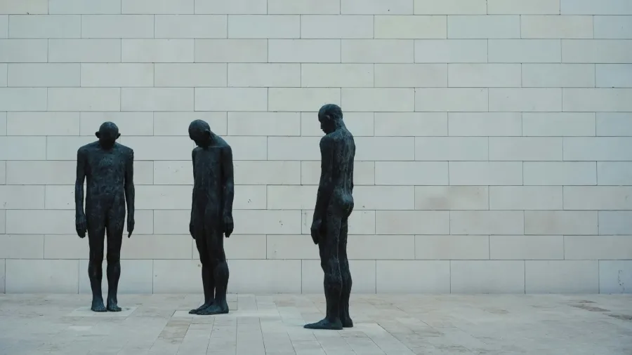 Drei Bronzefiguren stehen hintereinander vor einer hellen Steinwand