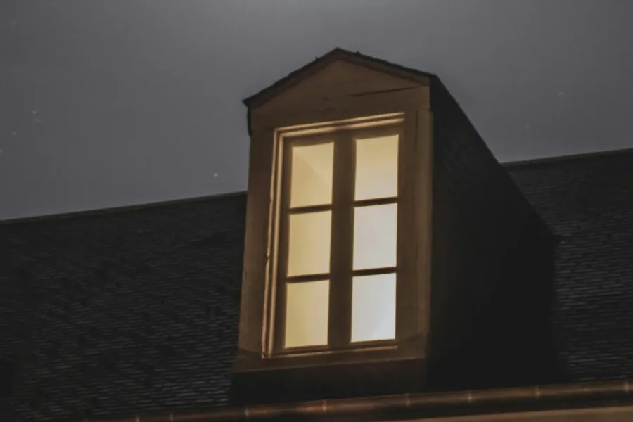 Ein einzelnes erleuchtetes Dachfenster in einer dunklen Nacht